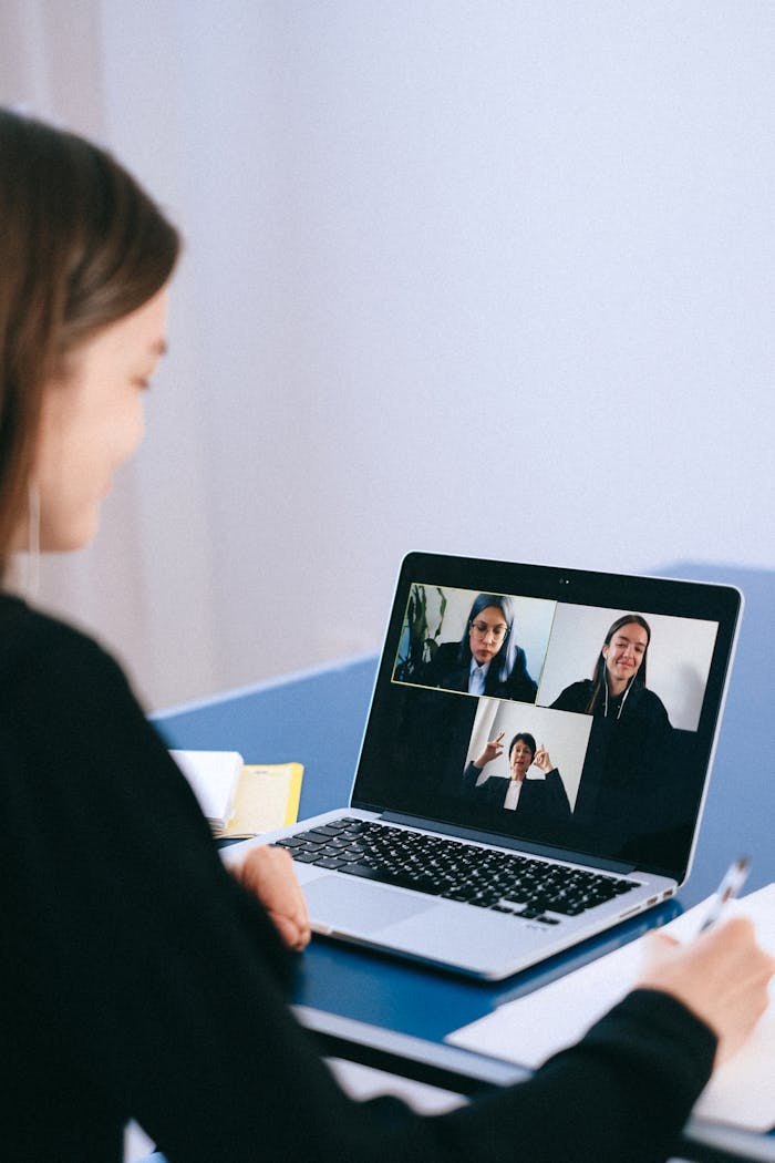 journey A woman participates in a virtual meeting with colleagues via video call on a laptop.
